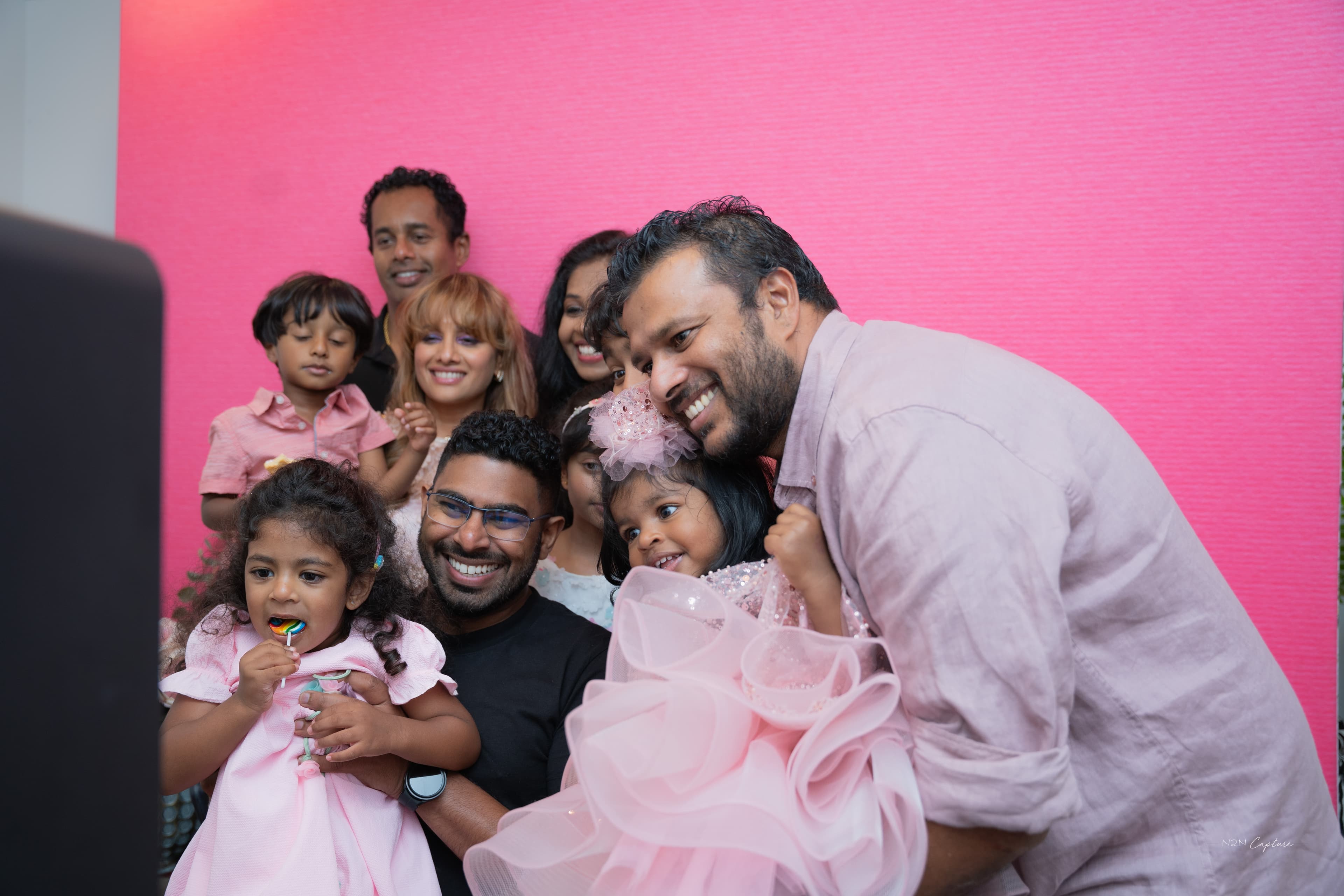 Family and children smiling together at a photo booth against a pink backdrop