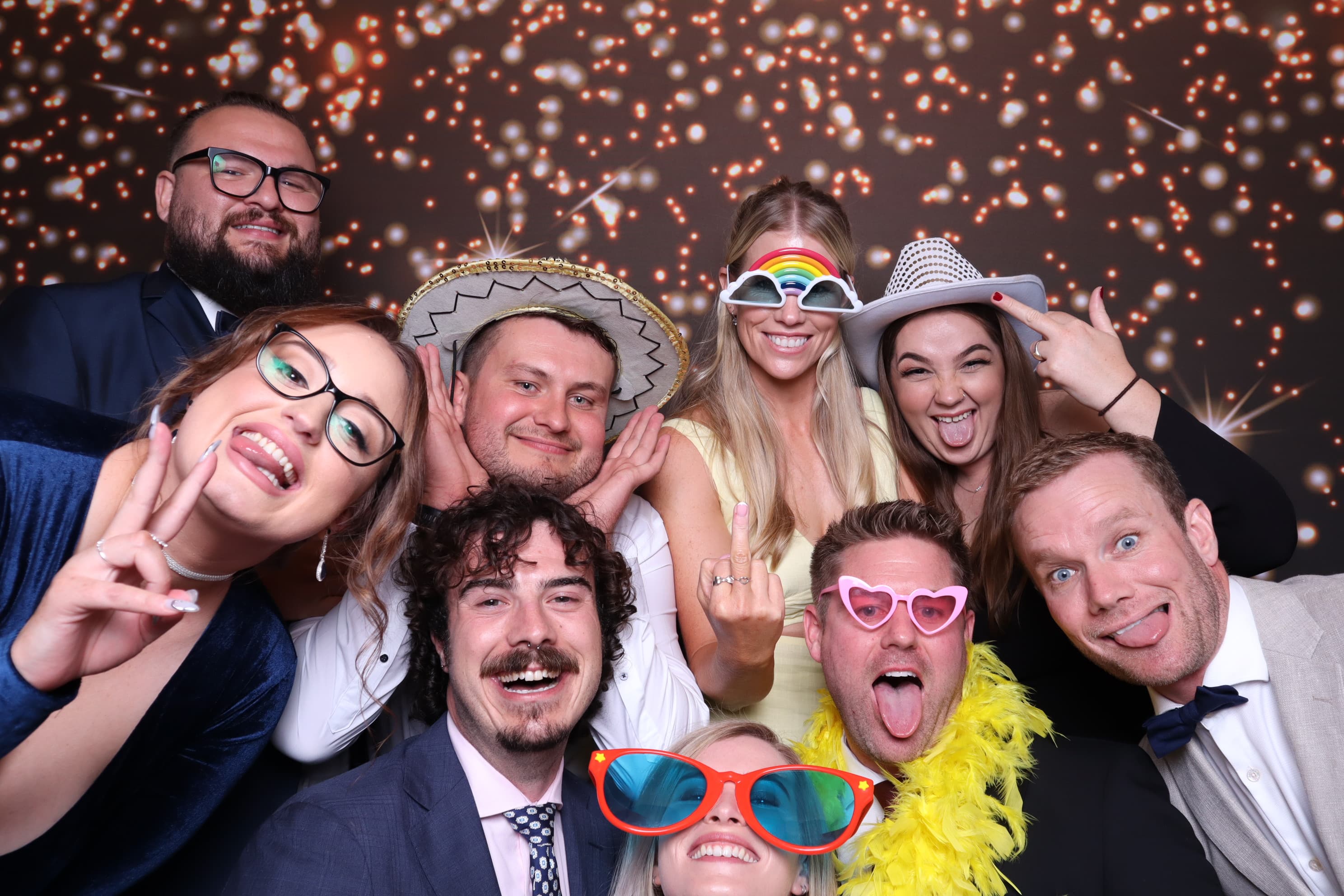 Guests posing with colourful glasses and hats against a sparkling gold backdrop