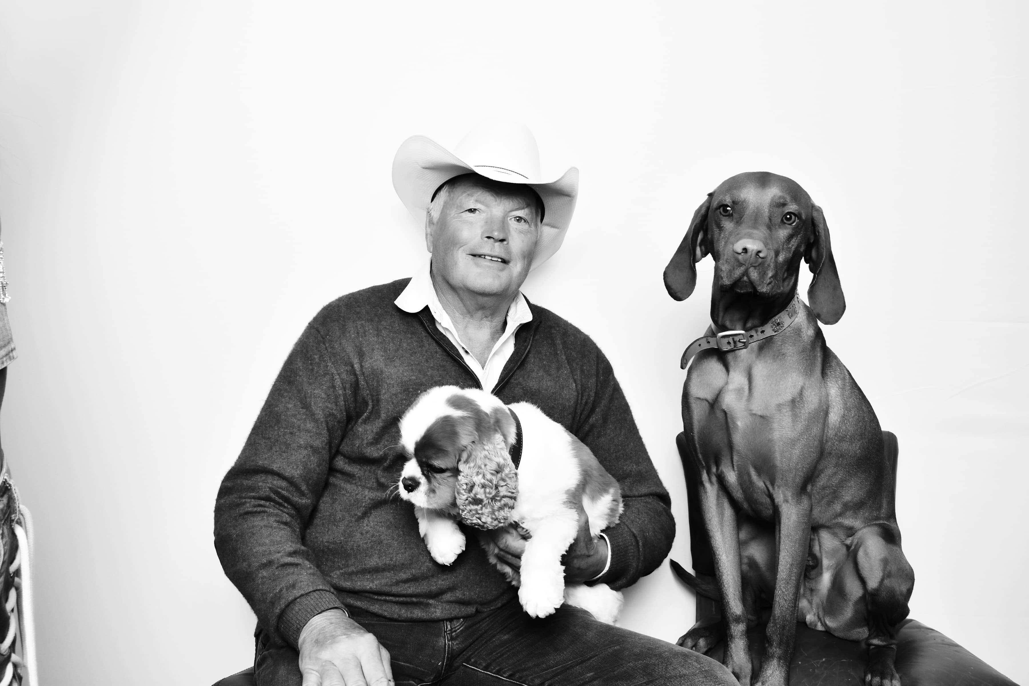 Black-and-white photo booth portrait of a man in a cowboy hat with two dogs